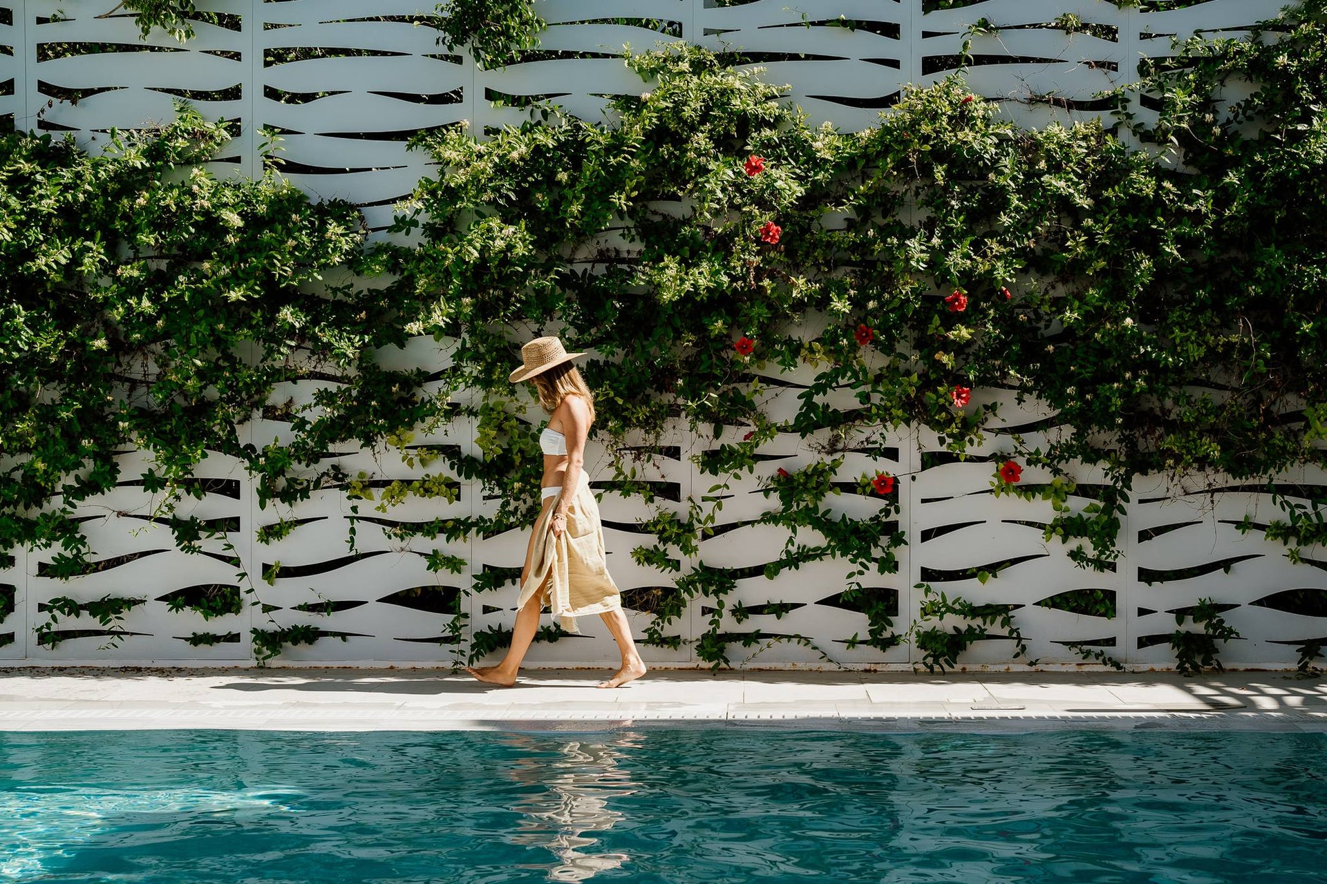 Woman walking by a pool with a decorative wall of greenery and flowers.